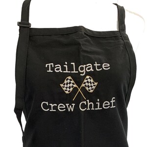 May include: Black apron with a white embroidered design that says "Tailgate Crew Chief" with two crossed checkered flags.