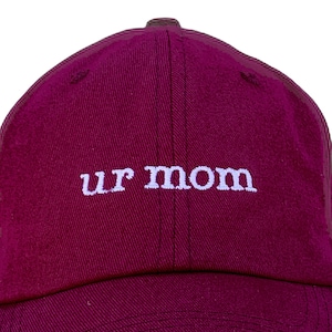 May include: A burgundy baseball cap with white embroidered text that reads "ur mom".