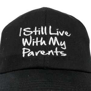 May include: A black baseball cap with white embroidered text that reads "I Still Live With My Parents".