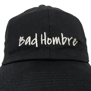 May include: A black baseball cap with a white embroidered inscription that reads "Bad Hombre".