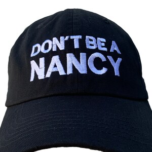May include: A black baseball cap with white embroidered text that reads "DON'T BE A NANCY".