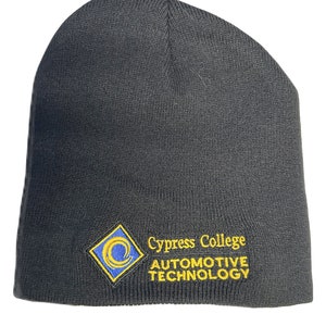 May include: A black knit beanie with the Cypress College Automotive Technology logo embroidered on the front. The logo is a blue and yellow diamond shape with the college name and program title in yellow text.