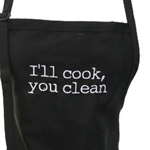 May include: Black kitchen apron with white embroidery that reads "I'll cook, you clean".