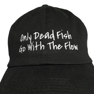 May include: Black baseball cap with white embroidered text that reads "Only Dead Fish Go With The Flow".