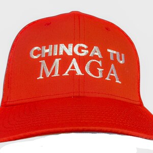 May include: Bright red baseball cap with the embroidered text "CHINGA TU MAGA" in white. The cap has a curved brim and a structured crown, suitable for casual wear.