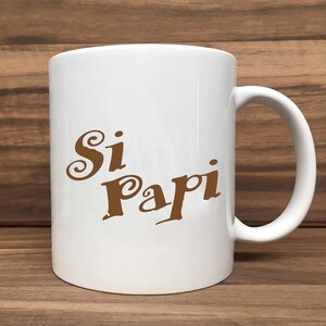 May include: White ceramic coffee mug with a brown inscription that reads "Si Papi".