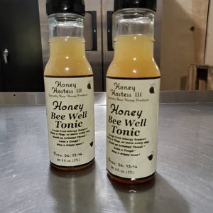 May include: Two 8-ounce bottles of Honey Bee Well Tonic, a honey-based cough and cold remedy. The bottles are labeled with the product name, ingredients, and dosage instructions. The bottles are clear glass with a yellow liquid inside.