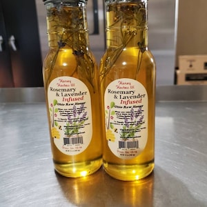 May include: Two glass bottles of honey infused with rosemary and lavender. The bottles are labeled "Honey Hostess LLC Rosemary & Lavender Infused Ohio Raw Honey" and have a product date of 24:13-14.