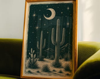 May include: Framed art print featuring a desert landscape with cacti under a starry night sky and a crescent moon. The artwork is in shades of green and beige, with a wooden frame. The print is displayed on a green sofa.