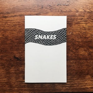May include: A white booklet with a black snake skin pattern and the word "SNAKES" in white text.
