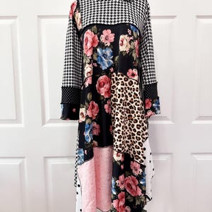 May include: A patchwork dress with a unique design. The dress features a houndstooth pattern, floral prints, leopard print, and polka dots. The dress has long sleeves and a round neckline. The color palette includes black, white, pink, and various floral colors.