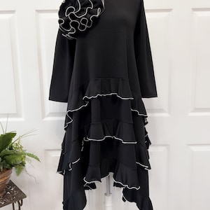 May include: Black dress with a large ruffled flower detail on the shoulder and multiple tiers of ruffles on the skirt.
