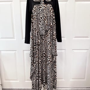 May include: A long-sleeved dress featuring a solid black upper bodice and a high neck with a matching tie. The lower portion of the dress displays a prominent leopard print pattern in shades of black, brown, and white, extending to the hem.