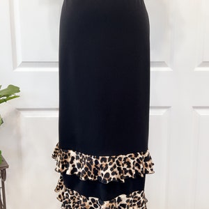 Puede incluir: Una falda midi negra con un dobladillo de doble volante con estampado de leopardo. La falda está hecha de una tela suave y fluida.
