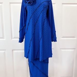 May include: A royal blue two-piece outfit with a long-sleeved top and a skirt. The top has a ruffled neckline and a large blue flower embellishment. Both pieces feature a black zig-zag trim.