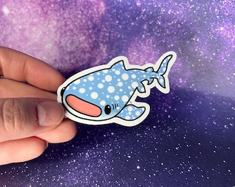 May include: A sticker featuring a cartoon whale shark with a light blue body and white polka dots. The whale shark has a pink mouth and black eyes. The sticker is outlined in black.