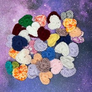 Puede incluir: Una colección de corazones tejidos a crochet en varios colores, incluyendo rojo, rosa, azul, verde y amarillo. Los corazones están dispuestos en un patrón circular, con el corazón más grande en el centro.