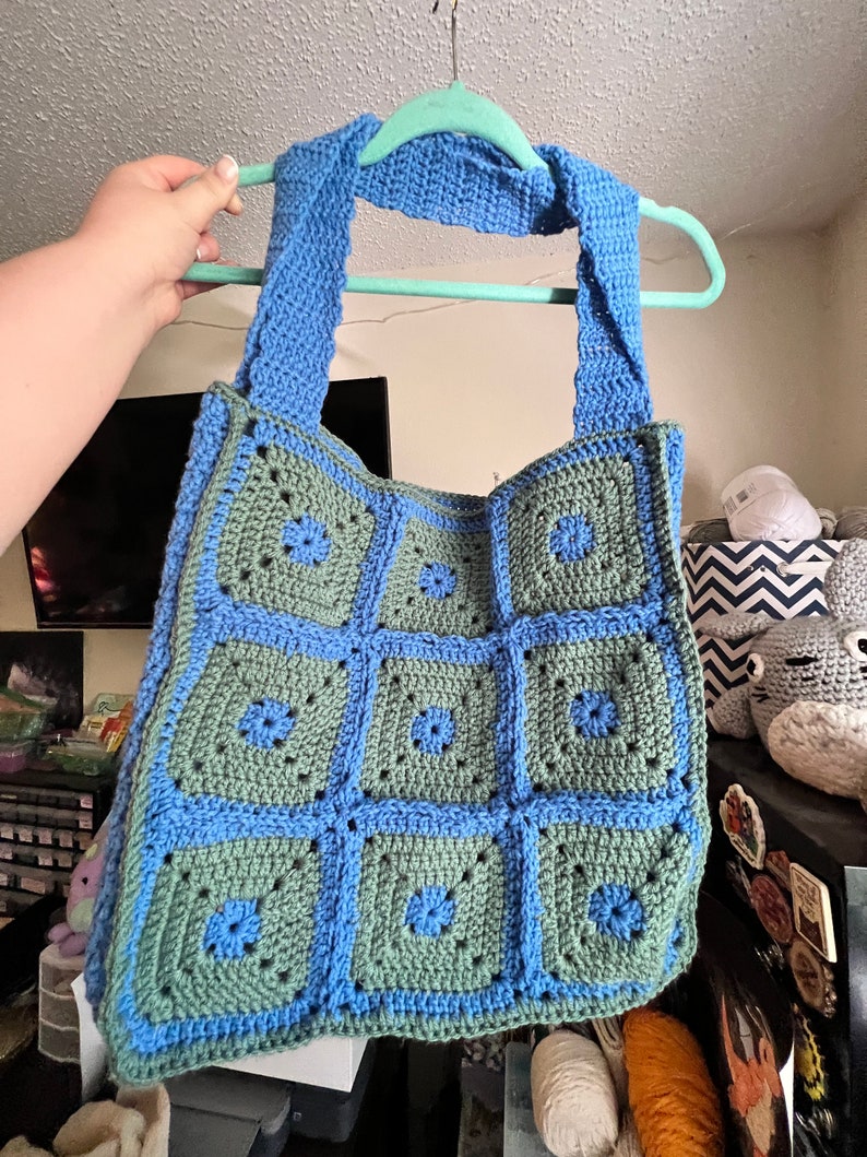 May include: A crocheted tote bag with blue and green squares. The bag has a blue crocheted strap.