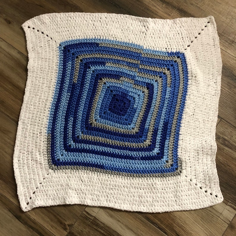 May include: A white crocheted baby blanket with a blue and gray square pattern in the center.