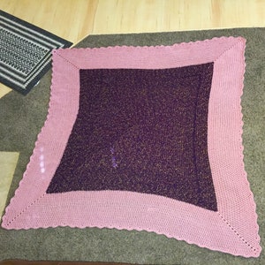 May include: A square crocheted throw blanket with a pink border and a purple center with gold glitter.