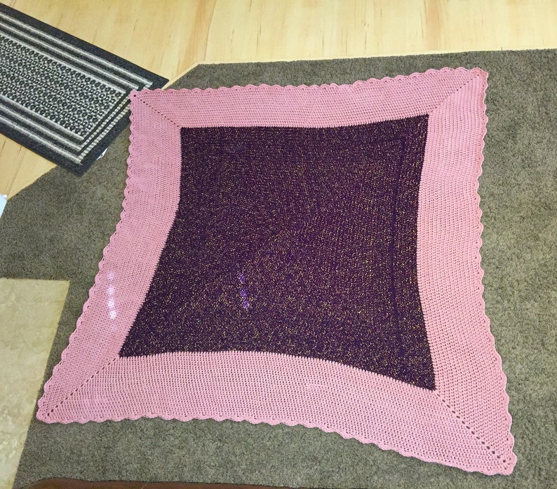 May include: A square crocheted throw blanket with a pink border and a purple center with gold glitter.