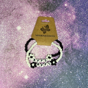 Puede incluir: Dos pulseras de cuentas negras y blancas con la palabra "BFFs" escrita en cuentas blancas. Las pulseras están en una tarjeta marrón con el texto "NESSIKNACKS0301" impreso en ella.
