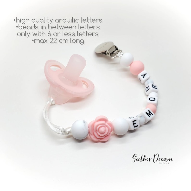 Peut inclure: Une sucette en silicone rose clair attach&eacute;e &agrave; une attache-sucette perl&eacute;e avec des perles rondes blanches et roses, une perle en forme de rose rose et des perles cubiques blanches avec des lettres noires formant le pr&eacute;nom EMORY.