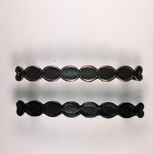 Könnte beinhalten: Zwei Schrankgriffe, einer in Schwarz und einer in Kupfer, mit einem dekorativen, gewellten Design.
