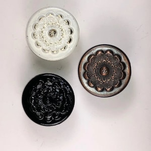 May include: Three decorative knobs with a floral design. The knobs are white, black, and copper.