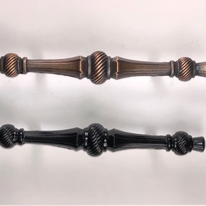 May include: Two cabinet pulls, one in a copper finish and one in black. Both pulls have a decorative, twisted design and a square shape at the end.