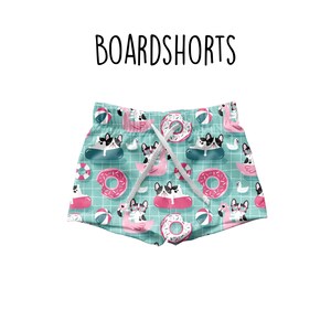 Puede incluir: Bañador azul turquesa con un patrón de bulldogs franceses montando flamencos rosas y donuts. El bañador tiene un cordón blanco.