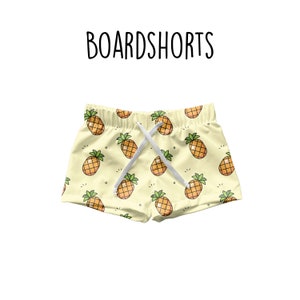 May include: Light yellow boardshorts with a repeating pattern of cartoon pineapples. The shorts have a white drawstring and the word "BOARDSHORTS" is printed in black above the shorts.