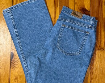 May include: Light blue denim jeans with a classic five-pocket design. The jeans have a straight leg cut and a faded wash. The back pocket features a small leather patch. The jeans are laid flat on a wooden surface.