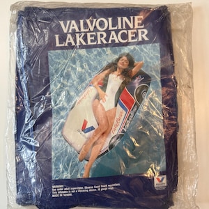 Puede incluir: Un flotador inflable azul Valvoline Lakeracer en su embalaje original. El flotador presenta un gráfico de una mujer con un traje de baño blanco descansando en el flotador en una piscina. El embalaje incluye el texto "VALVOLINE LAKERACER".