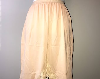 May include: Peach-colored slip with lace trim. The slip is made of a silky material and has a gathered waistband.