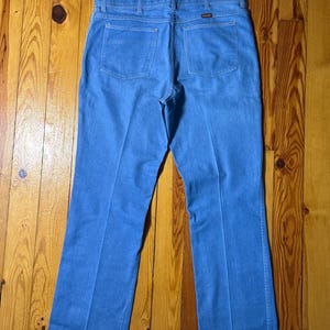 May include: A pair of blue denim jeans with a bootcut leg. The jeans have a brown leather patch on the back with the word "Wrangler" printed on it.