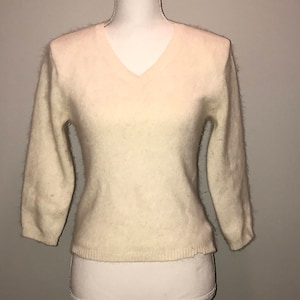 May include: A white, fluffy, v-neck sweater with long sleeves.