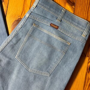 May include: A pair of light blue denim jeans with a back pocket and a Wrangler label.