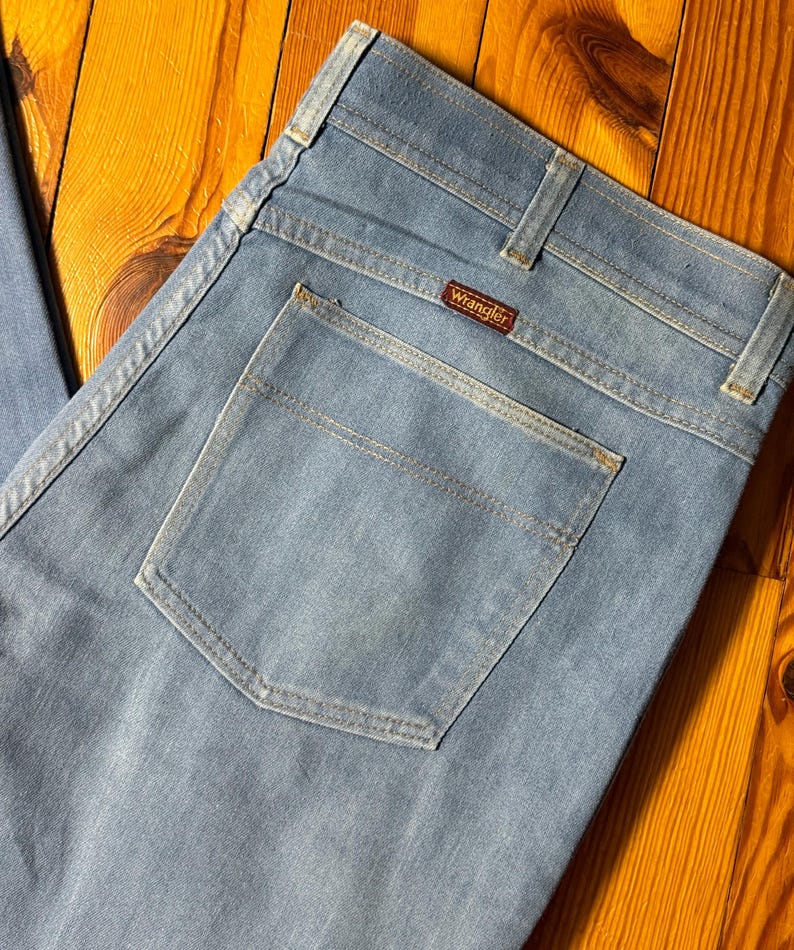 May include: A pair of light blue denim jeans with a back pocket and a Wrangler label.