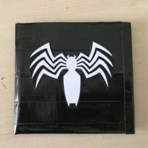 May include: Square black wallet with a white Venom emblem. The wallet's surface has a textured appearance, possibly duct tape. The Venom symbol is a stylized spider-like design.