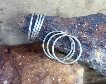 May include: A set of five silver rings stacked on top of each other. The rings are all hammered and have a textured finish. The rings are on a rock.
