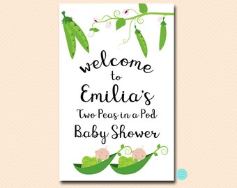 May include: A white welcome sign with green pea pods and flowers. The text reads "Welcome to Emilia's Two Peas in a Pod Baby Shower".