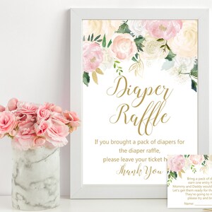 May include: A white frame with a floral design and gold lettering that reads "Diaper Raffle". The text below reads "If you brought a pack of diapers for the diaper raffle, please leave your ticket here. Thank you". A smaller card with a floral design and gold lettering reads "Bring a pack of nappies and earn one entry for a prize. Mummy and Daddy would appreciate any size! Let's get them ready for the changing to come. They're going to need a lot so please try and bring some!"