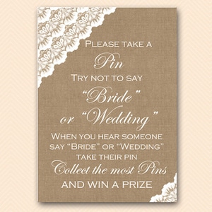 Può includere: Un cartello in juta con un bordo di pizzo bianco e il testo che recita "PLEASE TAKE A PIN TRY NOT TO SAY "BRIDE" OR "WEDDING" WHEN YOU HEAR SOMEONE SAY "BRIDE" OR "WEDDING" TAKE THEIR PIN COLLECT THE MOST PINS AND WIN A PRIZE"