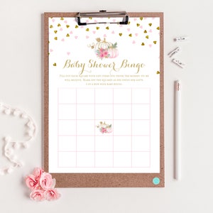 May include: A baby shower bingo game on a clipboard. The design features a gold and pink color scheme with a pumpkin and floral motif. The text "Baby Shower Bingo" is displayed in gold script.