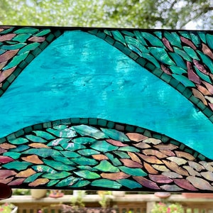 May include: A stained glass window panel with a turquoise blue wave design. The wave is made up of small, iridescent glass pieces in shades of pink, green, and blue.