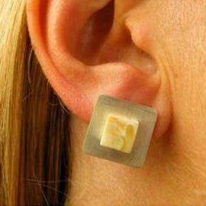 Puede incluir: Un par de pendientes cuadrados con una piedra marrón claro, veteada, engastada en un marco plateado.
