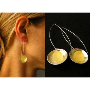 Puede incluir: Un par de pendientes de plata con una esfera de vidrio amarilla en el centro de cada pendiente.