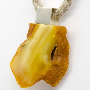 Pode incluir: Um pingente de &acirc;mbar amarelo com uma argola de prata, pendurado em um colar de corda marrom.