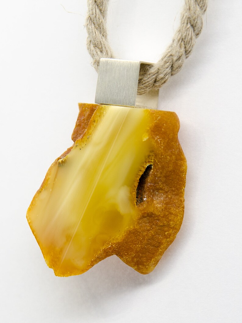 Pode incluir: Um pingente de &acirc;mbar amarelo com uma argola de prata, pendurado em um colar de corda marrom.